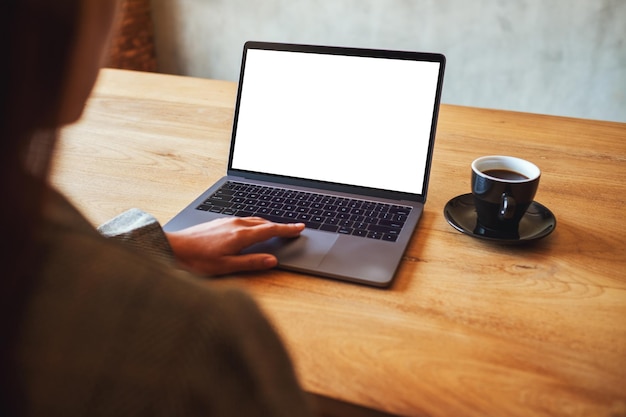 나무 테이블에 커피 컵이 있는 빈 흰색 데스크탑 화면이 있는 노트북 터치패드를 사용하고 만지는 여성의 흉내낸 이미지