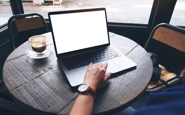 Mockup image of a woman using and touching on laptop touchpad with blank white desktop screen on wooden table