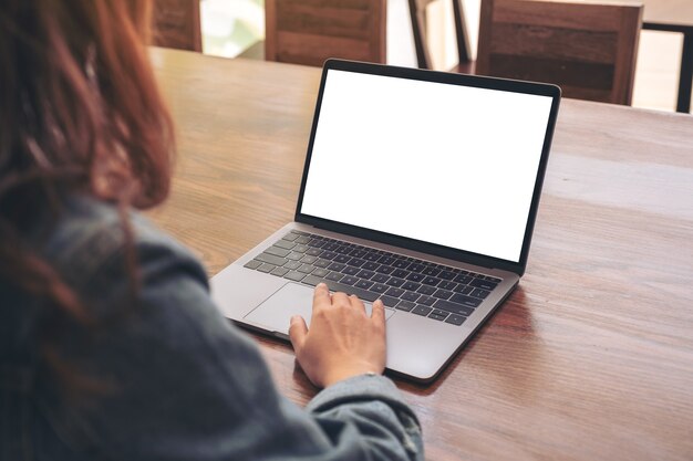 Mockup image of a woman using and touching on laptop touchpad with blank white desktop screen on wooden table