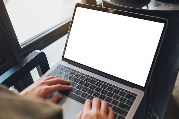 카페에 빈 흰색 바탕 화면이 있는 노트북 컴퓨터를 사용하고 타이핑하는 여성의 흉내낸 이미지