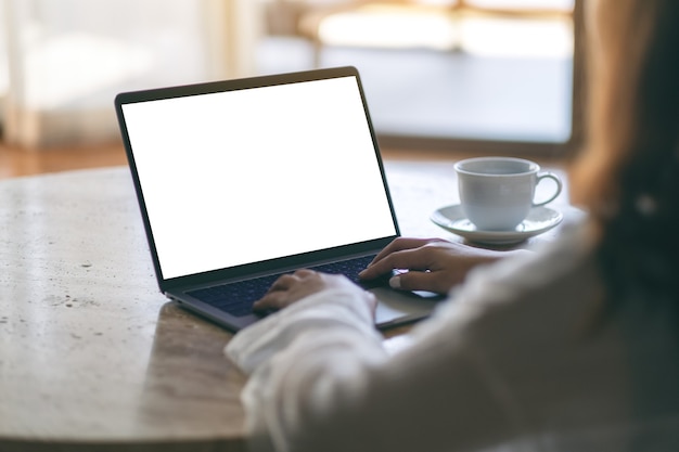 Mockup image of a woman using and typing on laptop with blank white desktop screen on the table while sitting on the floor in the house