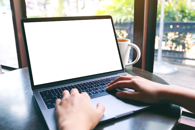 Immagine mockup di una donna che usa e digita sul laptop con uno schermo desktop bianco vuoto con una tazza di caffè sul tavolo