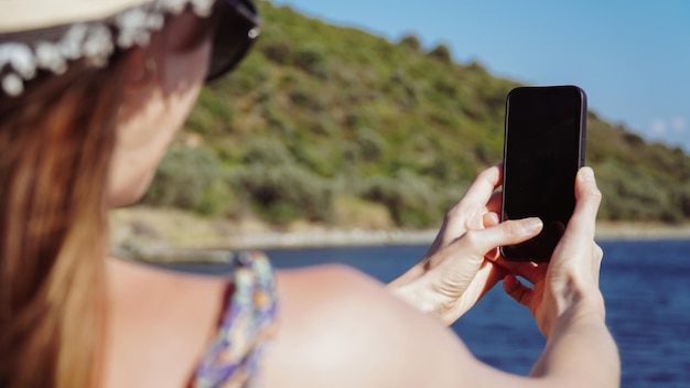 Foto immagine mockup di una donna che utilizza un telefono bianco nero con uno schermo desktop vuoto mentre scatta una foto.