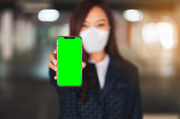 Мокап изображения женщины в защитной маске, показывающей мобильный телефон с пустым экраном для распространения концепции Covid-19