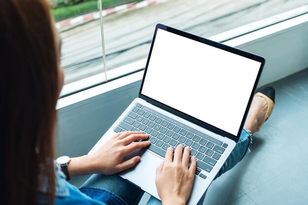 Mockup image of a woman working and typing on laptop computer with blank screen while sitting on the floor