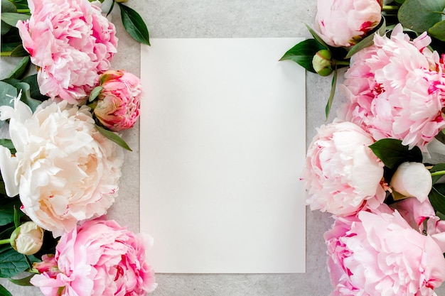 Фото Мокет приглашения пустая бумажная поздравительная карточка и пионы на сером каменном столе цветочный фон плоский вид сверху