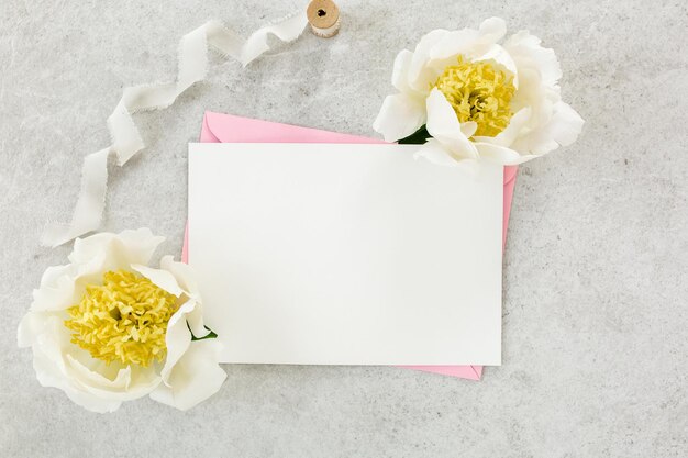 Foto invito a mock-up carta vuota biglietto di auguri busta rosa e peonie su tavolo di pietra grigia sfondo floreale vista superiore piatta