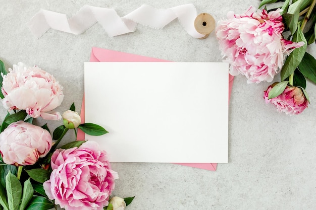 Mockup invitation blank paper greeting card pink envelope and peonies on gray stone table