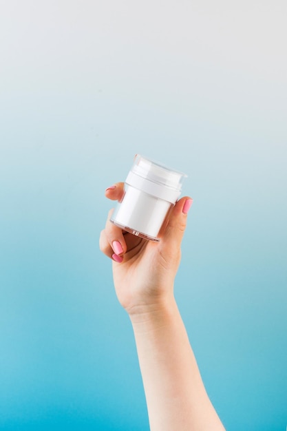 A mockup of a jar of moisturizer in a woman39s hand on a blue background
