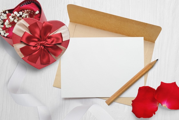 Mockup kraft envelope and a letter with a heart-shaped gift with a red bow and rose petals, greeting card for Valentines Day with place for your text. 