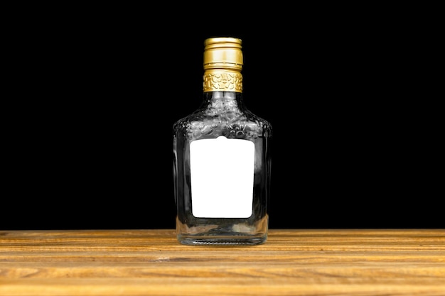 Mockup label on empty glass bottle of whiskey, cognac or vodka on a black background, wooden table. Template, copy space photo