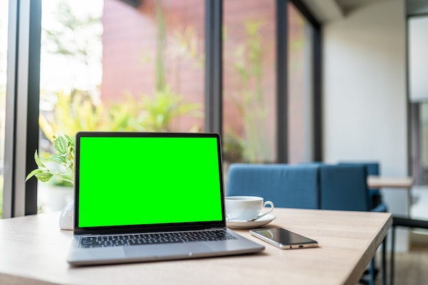 Mockup of laptop computer with empty screen with coffee cup and smartphone on table of the coffee shop background,Green screen