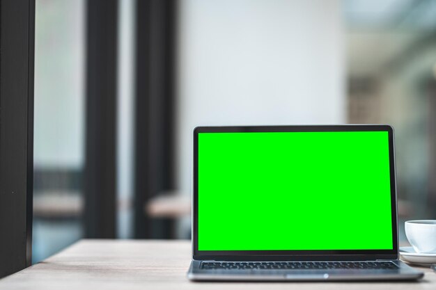 Modello di computer portatile con schermo vuoto con tazza di caffè e smartphone sul tavolo dello sfondo della caffetteria,schermo verde