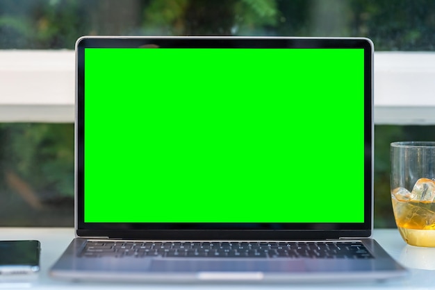 Mockup of laptop computer with empty screen with coffee cup and smartphone on table of the coffee shop background,Green screen