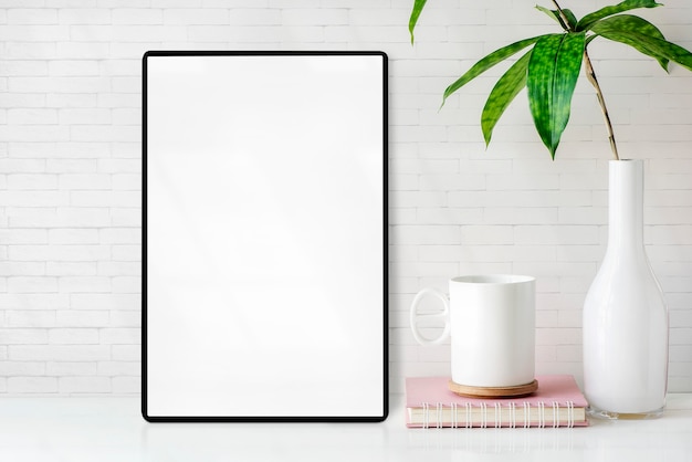 Mockup leeg scherm tablet met cup, boek en vaas met kamerplant op witte tafel