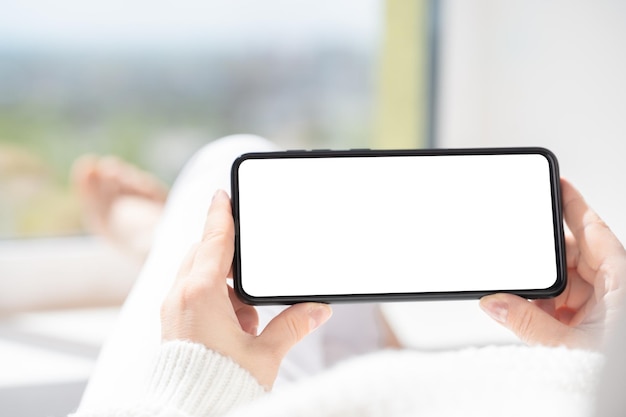 Mockup mobiele telefoon Vrouw ligt in ontspannen positie en kijkt naar video-inhoud op mobiele telefoon of mobiele smartphone met een wit leeg scherm dat de telefoon horizontaal houdt