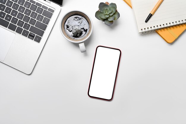 Mockup mobile phone with lank screen laptop coffee cup and notepad on white office desk