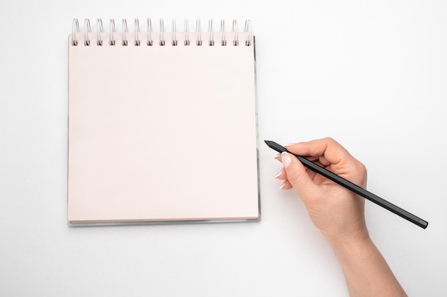 Mockup notepad woman hand with a pencil next to an empty blank\
white notepad women holding a pen writing a notebook recording\
concept