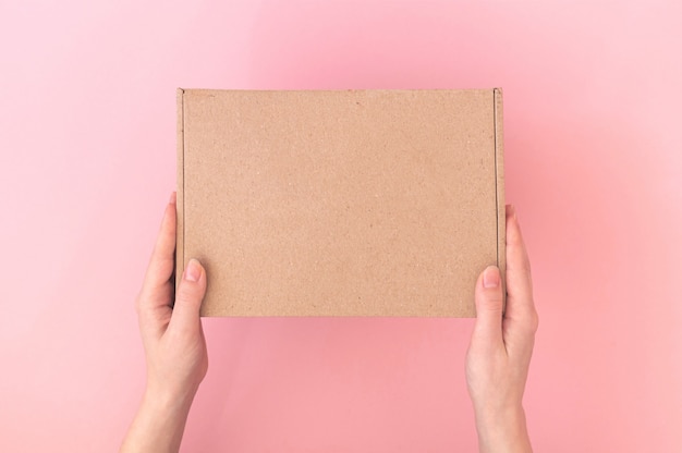 Картонная коробка посылки макета в руках мужчины доставки женщина на розовом пастельном фоне, стол, фото концепции службы доставки