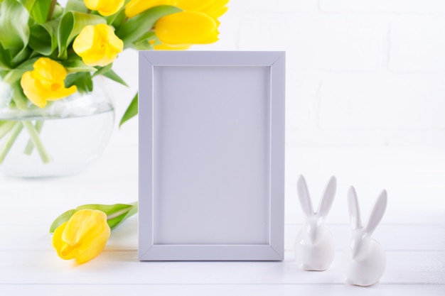Mockup of picture frame decorated yellow tulip flowers in vase on white background with clean space for text and design