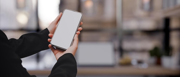 A mockup screen of a smartphone in a women's hands over blurred modern workspace in background