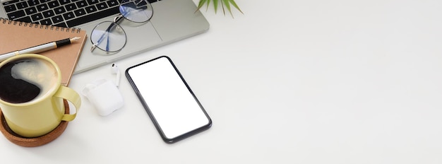 Mockup slimme telefoon met leeg scherm computer laptop koffiekopje en notebook op witte tafel met kopieerruimte