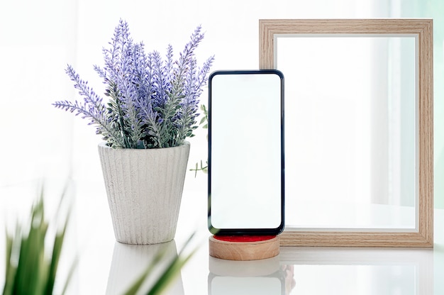 Foto smartphone modello con schermo bianco, cornice in legno e pianta d'appartamento