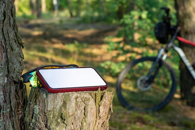 Mockup of a smartphone with a white display in the forest against the background of a mountain bike.