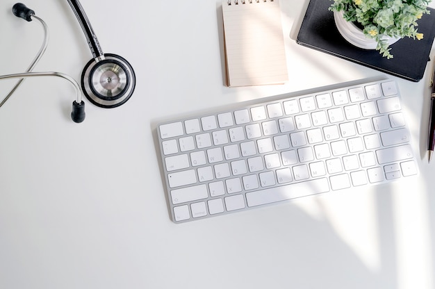 Mockup stethoscope with white keyboard and supplies on white table