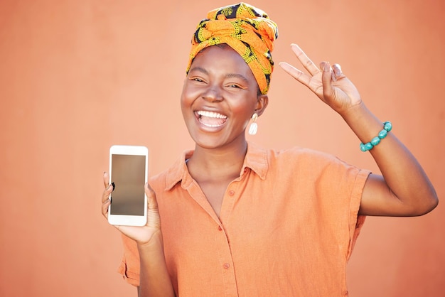 Mockup-telefoon of gelukkige zwarte vrouw met vredeshandgebaar tegen oranje muur met coole retro Afrikaanse mode Glimlachgezicht of opgewonden meisjesportret met scherm voor productplaatsing of marketing