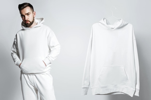 Photo mockup template man wearing white blank hoodie and other sample hanging nearby