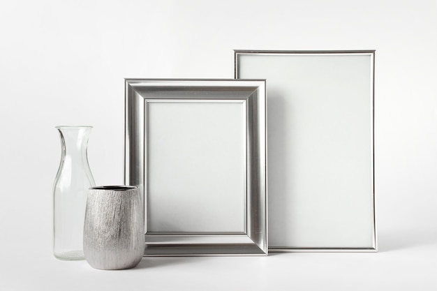 Mockup template with two blank silver frames, silver and glass small vases on white background.