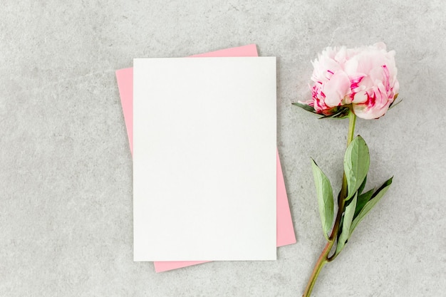 Mockup uitnodiging blanco papieren wenskaart roze envelop en pioenrozen op grijze stenen tafel Flower