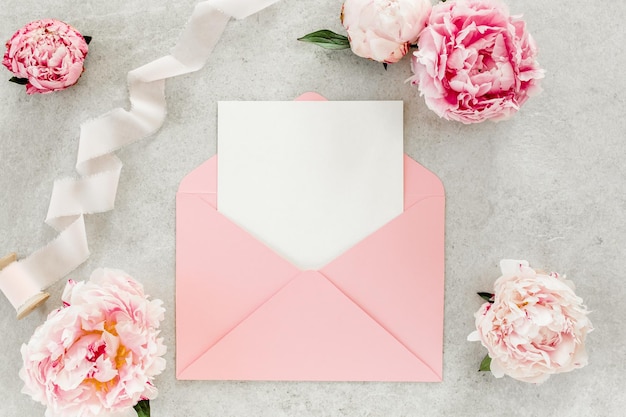 Mockup uitnodiging blanco papieren wenskaart roze envelop en pioenrozen op