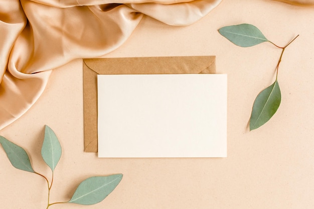 Mockup uitnodiging blanco wenskaart en ambachtelijke envelop groene bladeren eucalyptus plat bovenaanzicht