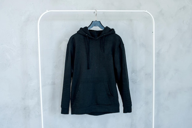 Mockup van een zwarte hoodiezak die aan een hanger hangt en in zijn handen een sweatshirt met plooien houdt