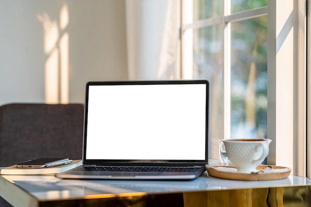 Mockup van laptopcomputer met leeg scherm met koffiekopje en smartphone op tafel naast het raam van de coffeeshop backgroundwhite scherm