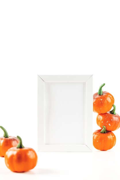 Mockup voor herfstuitnodigingskaart of ontwerp in wit frame naast oranje kleine pompoenen op een witte ...