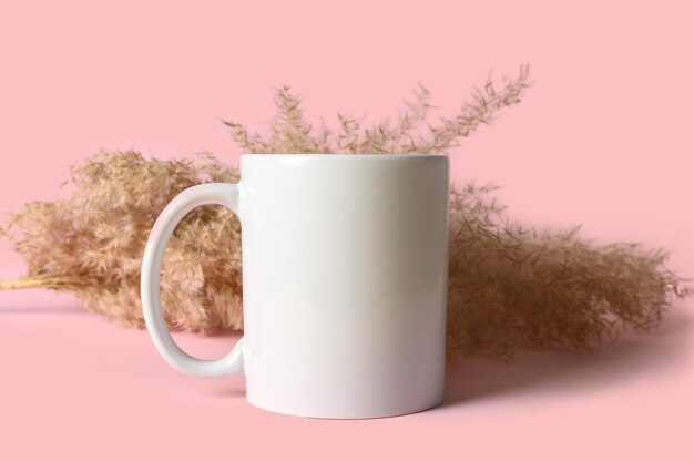 Mockup of a white caramic mug on a pink background Against the background of reeds