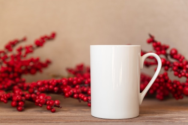 写真 モックアップ-クリスマスのヒイラギのベリーの背景に白いカップ。コーヒーまたは紅茶のマグカップ。