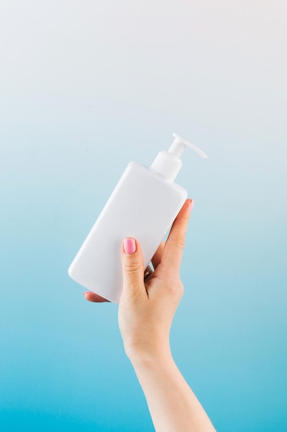 Un mockup di un dispenser bianco con un prodotto cosmetico in una mano di donna su sfondo blu