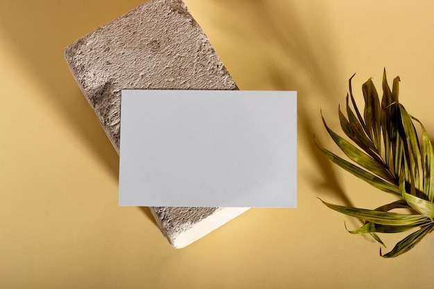 Mockup con carte di carta orizzontali vuote con spazio per la copia su un plinto con foglie di palma luce solare intensa e ombre su sfondo beige modello minimo per il layout aziendale vista dall'alto piatta