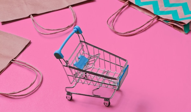 Mockup with shopping cart and paper bag on pink background. Happy customer concept. Internet shopping. Online store. Consumerism, lifestyle