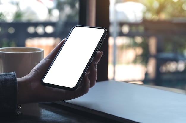 空白の白いデスクトップ画面で黒の携帯電話を持っている女性の手のモックアップ