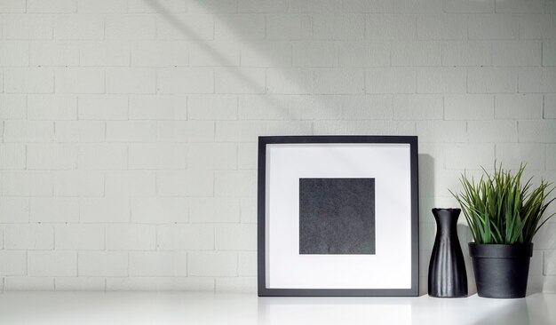 Mockup wooden frame, ceramic vase and houseplant on the table with brick wall.