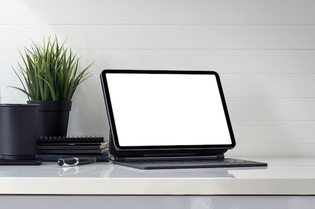 Mockup workspace with blank screen tablet and supplies on white table.