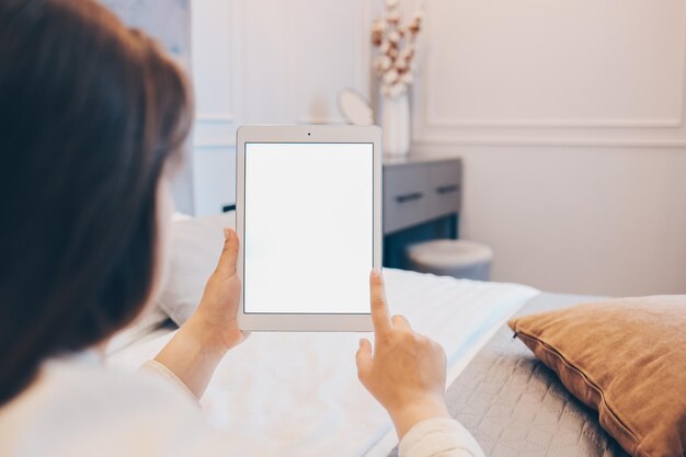 Mockupbeeld van de hand van de vrouw met witte tablet-pc met een leeg wit scherm thuis
