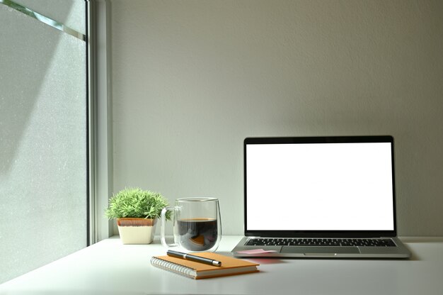 Mockuplaptop computer, koffie, notebook en pen met koffie in de buurt van windows.