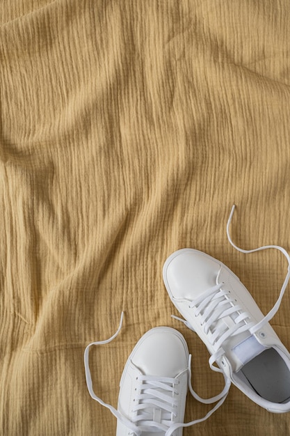 Mode blog of tijdschrift concept Witte vrouwelijke sneakers op gele verfrommelde mousseline doek achtergrond Plat lag bovenaanzicht minimale achtergrond