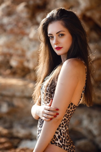 Mode buiten foto van mooi gebruind meisje met donker haar in luxe zwempak poseren op het strand van de zomer meisje in een zwembroek met een luipaardprint en het uiterlijk van een spaans of arabier